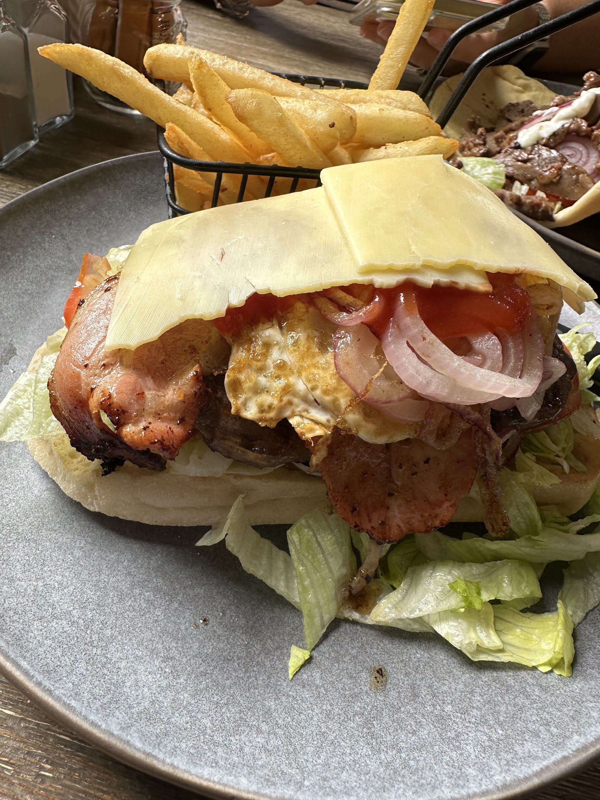 A loaded steak and bacon roll with egg, cheese and grilled onion, with a basket of chips