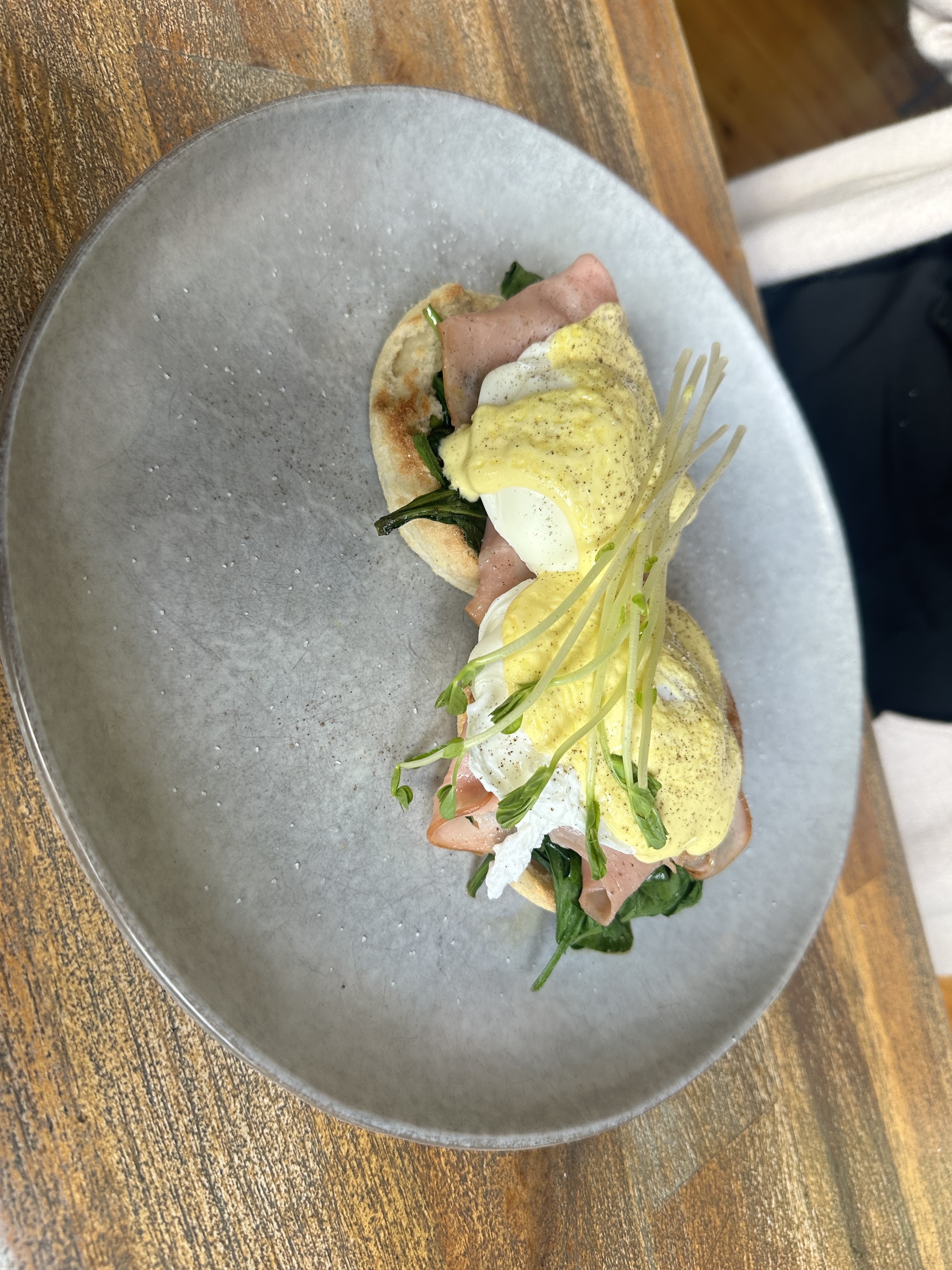 Eggs benedict on an English muffin with ham, spinach, hollandaise and pea shoots