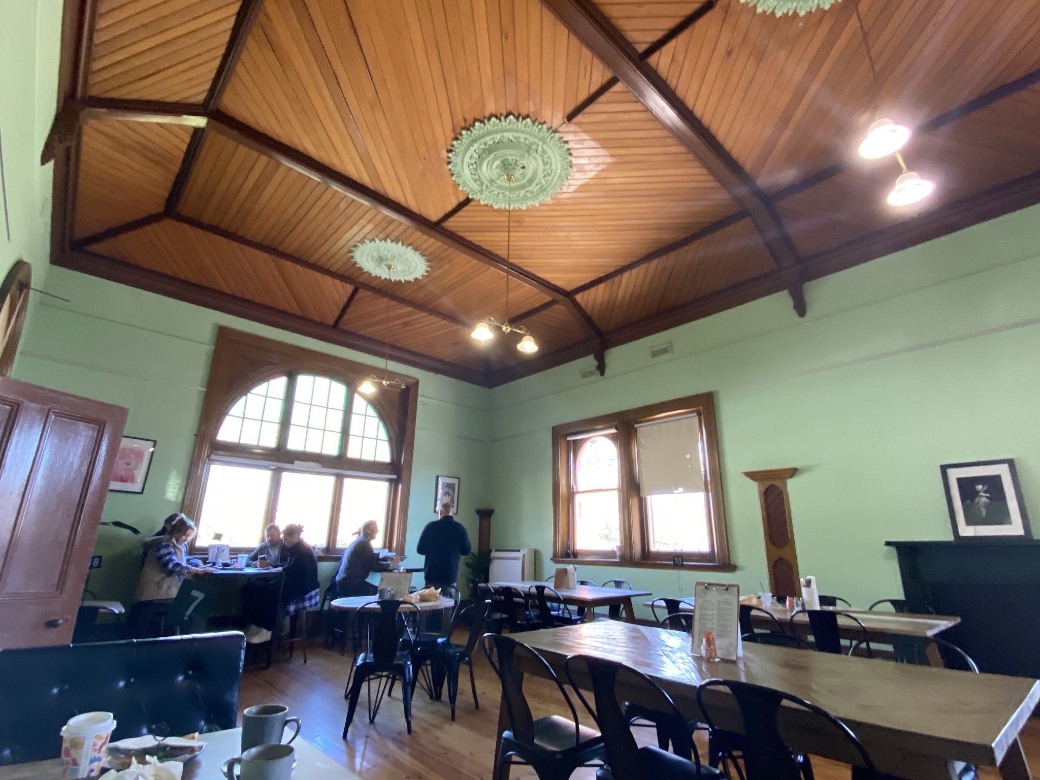 The main room at The Shire Cafe with customers at the window, long shared tables and the original timber ceiling